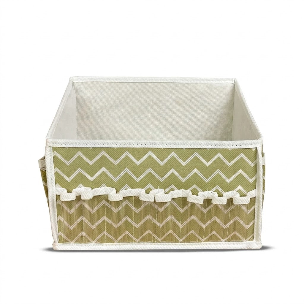 A square fabric storage basket with a sage green and white chevron pattern on the front, a white ruffled trim, and a cream-colored fabric lining, shown on a white background.