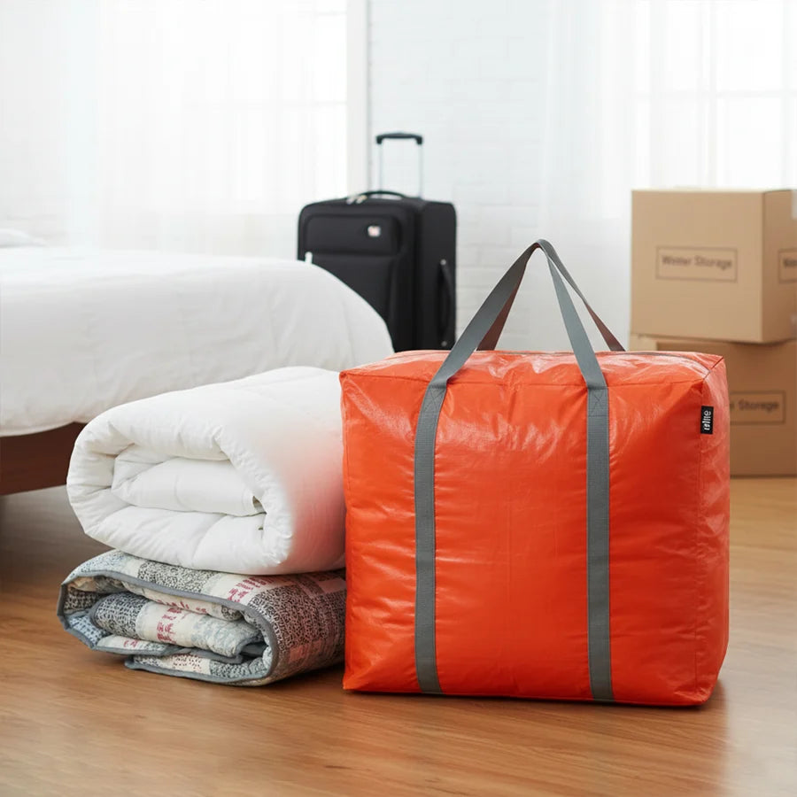 Orange folding bag next to folded clothes and a suitcase on a wooden floor.
