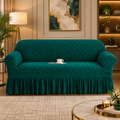 A plush, textured teal green sofa slipcover with a matching ruffled skirt, shown on a loveseat in a beautifully decorated living room.